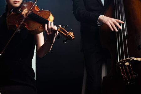 cropped view of professional musicians playing on violin and contrabass on dark stageの写真素材