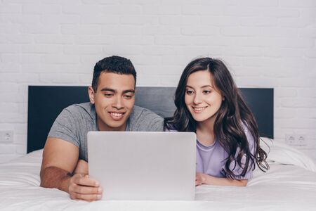bi-racial man and attractive woman networking while using laptop in bedroomの写真素材