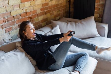 KYIV, UKRAINE - APRIL 29, 2020: cheerful woman holding joystick while playing video game in living roomの写真素材