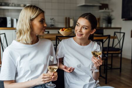 Smiling sisters talking while holding glasses of wine at homeの写真素材
