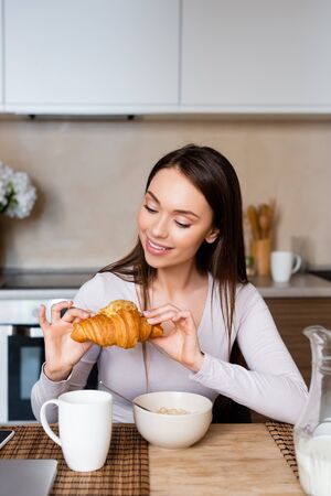cheerful girl looking at tasty croissant near bowl and cupの写真素材