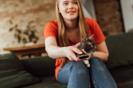 selective focus of happy girl holding remote controller near cute catの写真素材