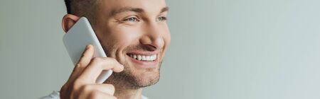 Horizontal crop of smiling man talking on smartphone isolated on grey