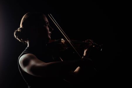 silhouette of female musician playing on violin on dark stageの写真素材