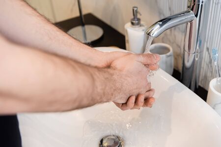 Cropped view of man washing hands in bathroom