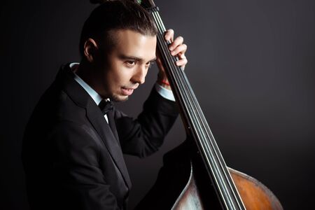 young professional musician playing on double bass on dark stageの写真素材
