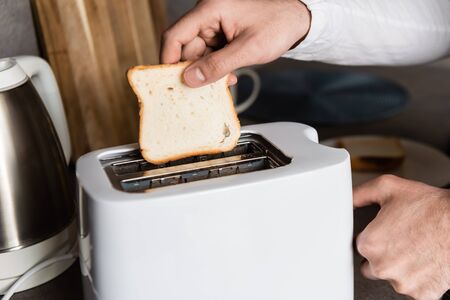 cropped view of man putting piece of bread into toaster