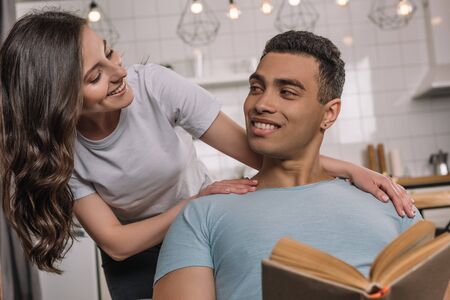 selective focus of handsome mixed race man holding book near attractive girlfriendの写真素材
