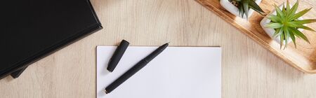 top view of green plants, black notebooks, white paper with pen on wooden surface, panoramic shotの写真素材