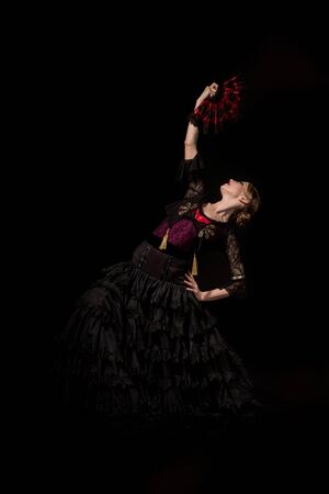 pretty flamenco dancer with hand on hip holding fan and dancing isolated on black の写真素材