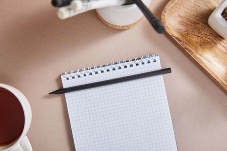 top view of cup of tea, blank notebook with pencils on beige surface, selective focus