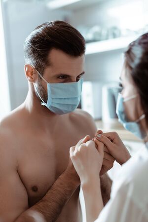 selective focus of young couple in medical masks holding hands in kitchenの写真素材