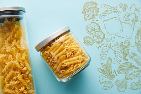 top view of raw penne and fusilli  in jars on blue background with food illustrationの写真素材