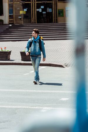 Selective focus of courier with backpack walking on road crosswalk