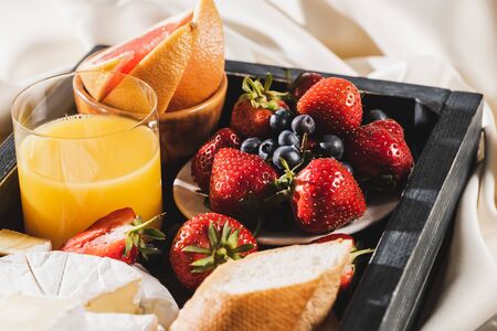close up view of french breakfast with grapefruit, Camembert, orange juice, berries and baguette on wooden trayの写真素材