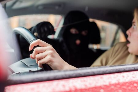 Selective focus of scared driver looking at robber with knife in car