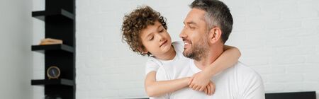 panoramic shot of curly son hugging happy bearded father in bedroom