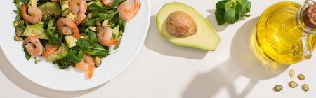 top view of fresh green salad with pumpkin seeds, shrimps and avocado on plate near ingredients on white background, horizontal imageの写真素材