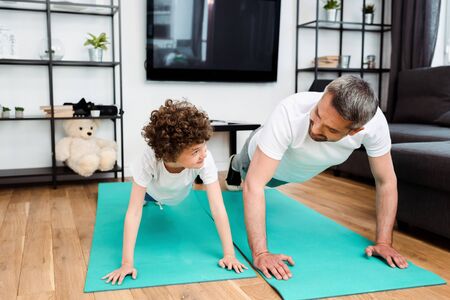 handsome father and curly son exercising on fitness mats and looking at each otherの写真素材
