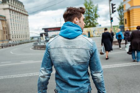 Back view of man in earphones walking on crosswalk on urban street