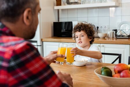 selective focus of father and son clinking glasses of orange juiceの写真素材