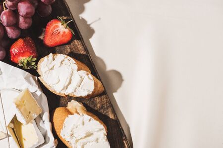 top view of of french breakfast with baguette, Camembert, strawberries and grape on wooden cutting board on white tableclothの写真素材