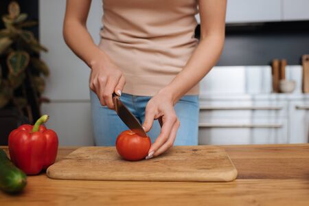 cropped view of young woman cutting fresh tomato on chopping boardの写真素材