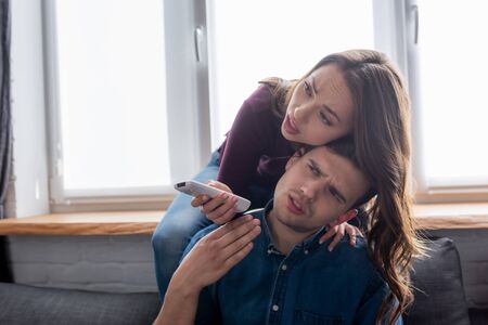displeased man near woman holding remote controller from air conditioner while feeling hotの写真素材