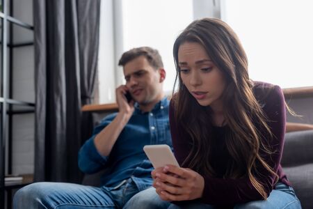 selective focus of girl texting while holding smartphone and man talking in living room