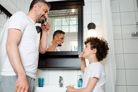 handsome father and curly son brushing teeth in bathroomの写真素材