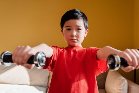 selective focus of sportive asian boy exercising with dumbbells at home during quarantine