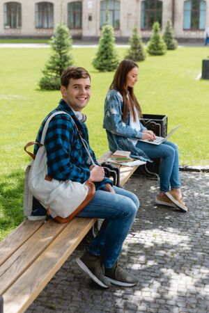selective focus of happy student smiling while girl using laptop near university campus, online study conceptの写真素材