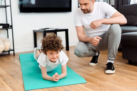 bearded father looking at curly son exercising on fitness matの写真素材