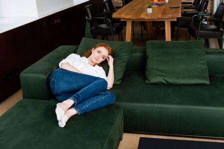 Sad woman looking at camera while lying on sofa at homeの写真素材