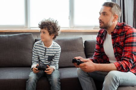 handsome father and curly son playing video game in living room