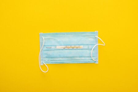 top view of medical mask and thermometer on yellow backgroundの写真素材