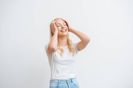 excited girl touching head while laughing with closed eyes isolated on whiteの写真素材