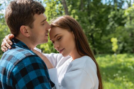 cheerful girl with closed eyes hugging handsome boyfriendの写真素材