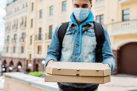 Selective focus of delivery man in medical mask holding pizza boxes with urban street at backgroundの写真素材
