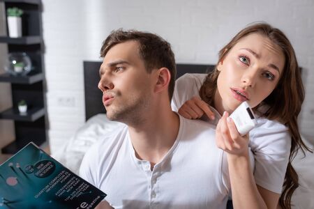 displeased man holding magazine while feeling hot near woman with remote controller from air...