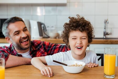 selective focus of cheerful father looking at cute and curly son near breakfast on table