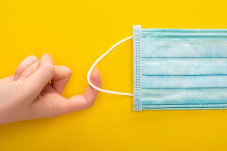 cropped view of woman holding medical mask on yellow background