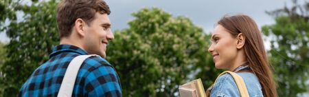 panoramic crop of happy and young woman holding books and looking at handsome studentの写真素材
