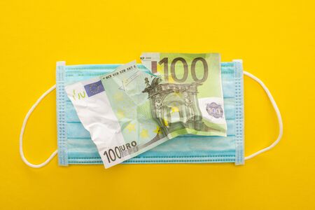 top view of torn euro banknote and medical mask on yellow backgroundの写真素材