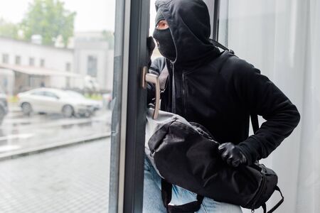 Robber in balaclava and leather gloves holding bag near open windowの写真素材