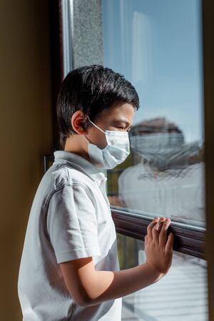 asian boy in medical mask looking through window on quarantineの写真素材