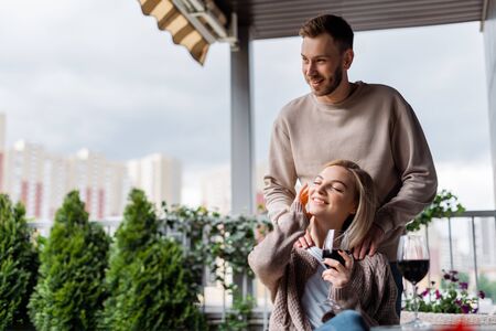 selective focus of happy man standing near happy girl with closed eyes holding glass of red wineの写真素材