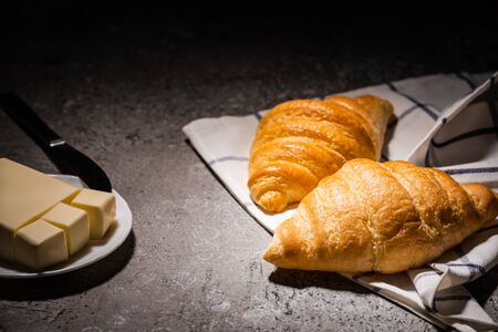 fresh baked croissants on towel near butter and knife on concrete grey surface in darkの写真素材