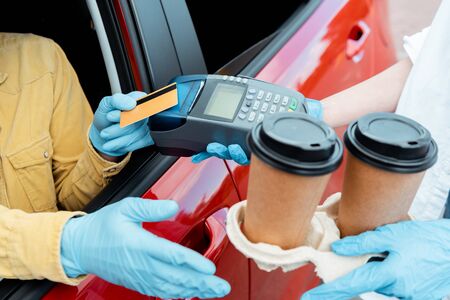 cropped view of man in protective gloves making transaction with credit card and terminal to buy takeaway coffee from car during covid-19 pandemicの写真素材