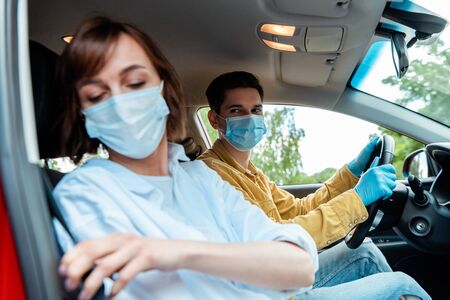 man and woman in medical masks and protection gloves sitting in car during coronavirus pandemic, selective focusの写真素材